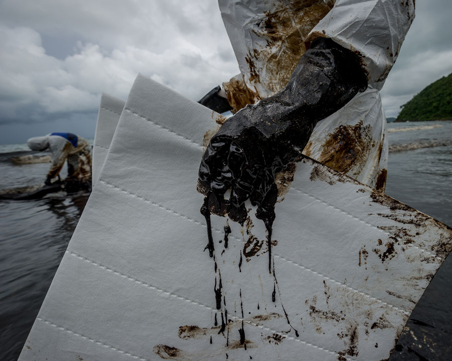 people in white safety suits cleaning up oil spill